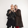 Two fashionable girlfriends in oversized fashionable youth clothes in studio. Attractive girl in leather jacket stands with