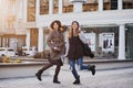 Two fashionable joyful smiling girls jumping over city background. Stylish look, travelling together, wearing modern