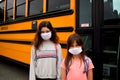 Coronavirus school:Two female children wearing facemasks in front of a school bus