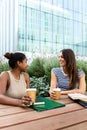 Two female college girl friends laughing, talking and drinking coffee outdoors in university campus park. Vertical. Royalty Free Stock Photo