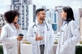 Two female doctors and a male colleague standing on the balcony outside a hospital smiling and having a conversation Royalty Free Stock Photo