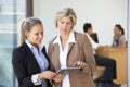 Two Female Executives Looking At Tablet Computer With Office Meeting In Background Royalty Free Stock Photo