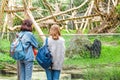 Female friends with backpacks are watching at the zoo for a chimpanzee monkey. The concept of zoological students or leisure