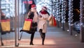 Two female friends in Christmas hats having fun shopping for Xmas outside a mall Royalty Free Stock Photo