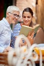 Two female friends of different generations reading a book together while they have a drink in the bar. Leisure, bar, friendship,