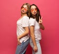 Two female friends hugging and having fun together, showing peace gesture while looking at camera, isolated over pink Royalty Free Stock Photo