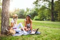 Two female friends sitting on the grass, talking and using laptop Royalty Free Stock Photo