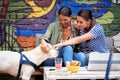 Two female friends sitting in outdoor cafe, smiling, playing with a dog Royalty Free Stock Photo