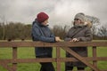 Two female friends talking outdoors leaning on a wooden fence Royalty Free Stock Photo