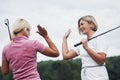 Two female golf players giving high five in the background of beautiful green woods