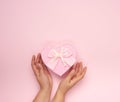 Two female hands hold a paper closed pink box in the shape of a heart on a pink background Royalty Free Stock Photo