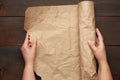 Two female hands hold a rolled roll of brown craft paper on a wooden table Royalty Free Stock Photo