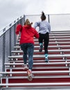 Two female high school athletes running up bleachers