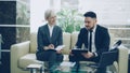 Two female and male business colleagues with clipboard and notepad talking at hotel lobby. Luggage in near couch Royalty Free Stock Photo