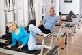 Young woman and mature couple using bed of Pilates reformer bed equipment while training together in wellness center Royalty Free Stock Photo