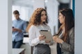 Two female managing directors discussing ideas of project on digital tablet while walking down in office hall, confident women