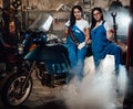 Two female mechanic posing next to a sportbike in authentic workshop garage surrounded by smoke