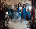 Two female mechanic posing next to a sportbike in authentic workshop garage surrounded by smoke