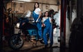 Two female mechanic posing next to a sportbike in authentic workshop garage