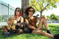 Two female musicians sitting by tree playing music