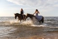 Female riders galloping on horseback through the shallow waters of a coastal beach Royalty Free Stock Photo