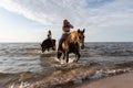 Female riders galloping on horseback through the shallow waters of a coastal beach Royalty Free Stock Photo