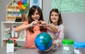 Two female students showing globe world earth while one making heart shape with hands Royalty Free Stock Photo