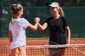 Two female tennis players shaking hands with smiles on a sunny day, exuding sportsmanship and friendship after a