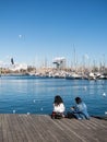 Two female tourists rest surrounded by seagulls in the old port of the city of Barcelona. Catalonia, Spain
