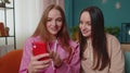 Two female woman friends family watching funny movies on smartphone, online comedy film at home