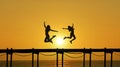 Two females in silhouette jump on a sunset pier Royalty Free Stock Photo