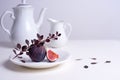 Two figs on a white plate with a branch of barberry, white teapot and cup on the table Royalty Free Stock Photo