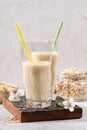 Two figured glasses with healthy oats milk on brown burned  board and jar of oaty flakes on light background Royalty Free Stock Photo