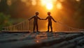 Two figures shake hands across a bridge at sunset. They represent teamwork and connection, building bridges between people and Royalty Free Stock Photo