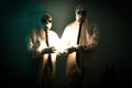 Two figures wearing biohazard suits hold a strange light