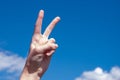 Two fingers of a caucasian woman hand showing victory or peace gesture on blue sky background. Copy space Royalty Free Stock Photo