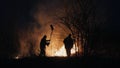 Two firefighters with fire flappers extinguish a fire in the forest at night Royalty Free Stock Photo