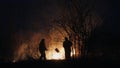 Two firefighters with fire flappers extinguish a fire in the forest at night Royalty Free Stock Photo