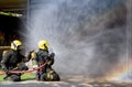 Two firefighters sit on floor and spray of water with curtain shape and rainbow reflex occur on water aerosol in front of Royalty Free Stock Photo