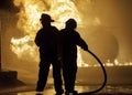 Two firefighters standing in front of a fire with hose