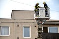 Two firefighters uprise into telescopic boom basket of fire truck, block of flats in background