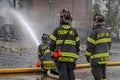 Two firefighters watch a third fireman spraying water on a store in a strip mall that was destroyed in a fire at a strip mall