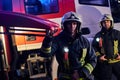 Two brave firemen wearing a protective uniform standing next to a fire truck. Arrival on call at night time Royalty Free Stock Photo