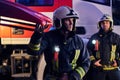 Two brave firemen wearing a protective uniform standing next to a fire truck. Arrival on call at night time Royalty Free Stock Photo