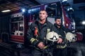 Two firemen wearing protective uniform standing next to a fire truck in a garage of a fire department. Arrival on call Royalty Free Stock Photo