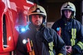 Two firemen wearing protective uniform standing next to a fire truck in a garage of a fire department. Royalty Free Stock Photo