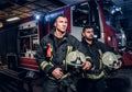 Two firemen wearing protective uniform standing next to a fire truck in a garage of a fire department. Arrival on call Royalty Free Stock Photo