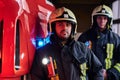 Two firemen wearing protective uniform standing next to a fire truck in a garage of a fire department. Royalty Free Stock Photo