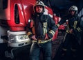 Two firemen wearing protective uniform standing next to a fire truck in a garage of a fire department. Royalty Free Stock Photo