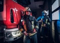 Two firemen wearing protective uniform standing next to a fire truck in a garage of a fire department. Royalty Free Stock Photo